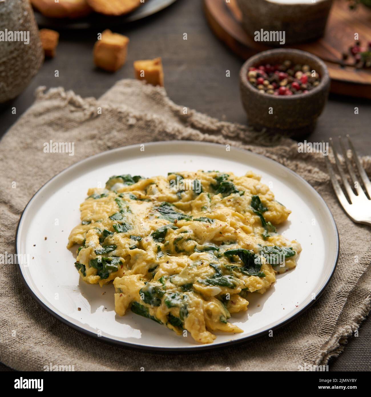 Scrambled eggs with spinach, cup of tea on dark brown background Stock Photo