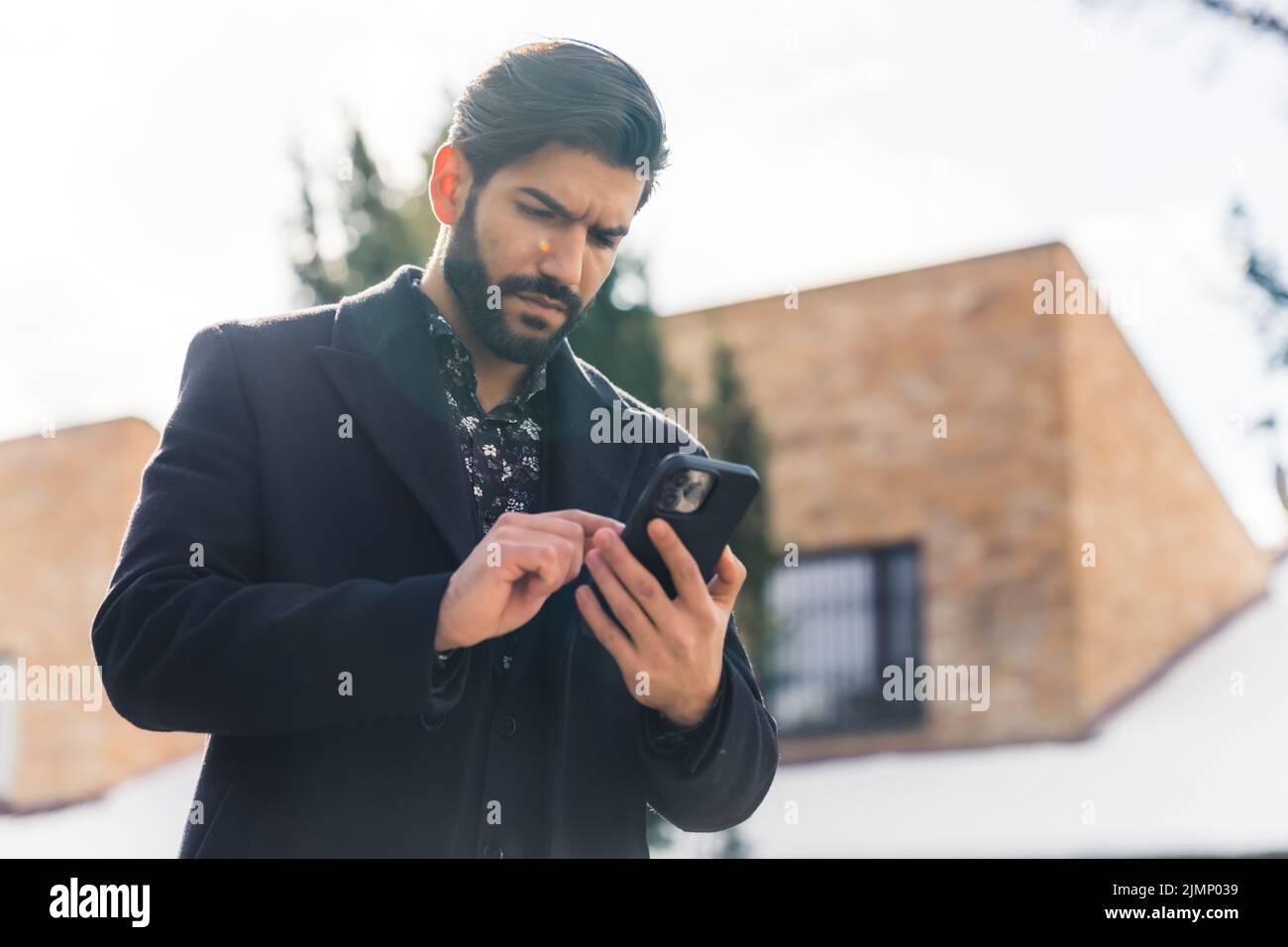 Hispanic bearded businessman wearing coat outside on winter morning swiping through messages on smarphone. High quality photo Stock Photo