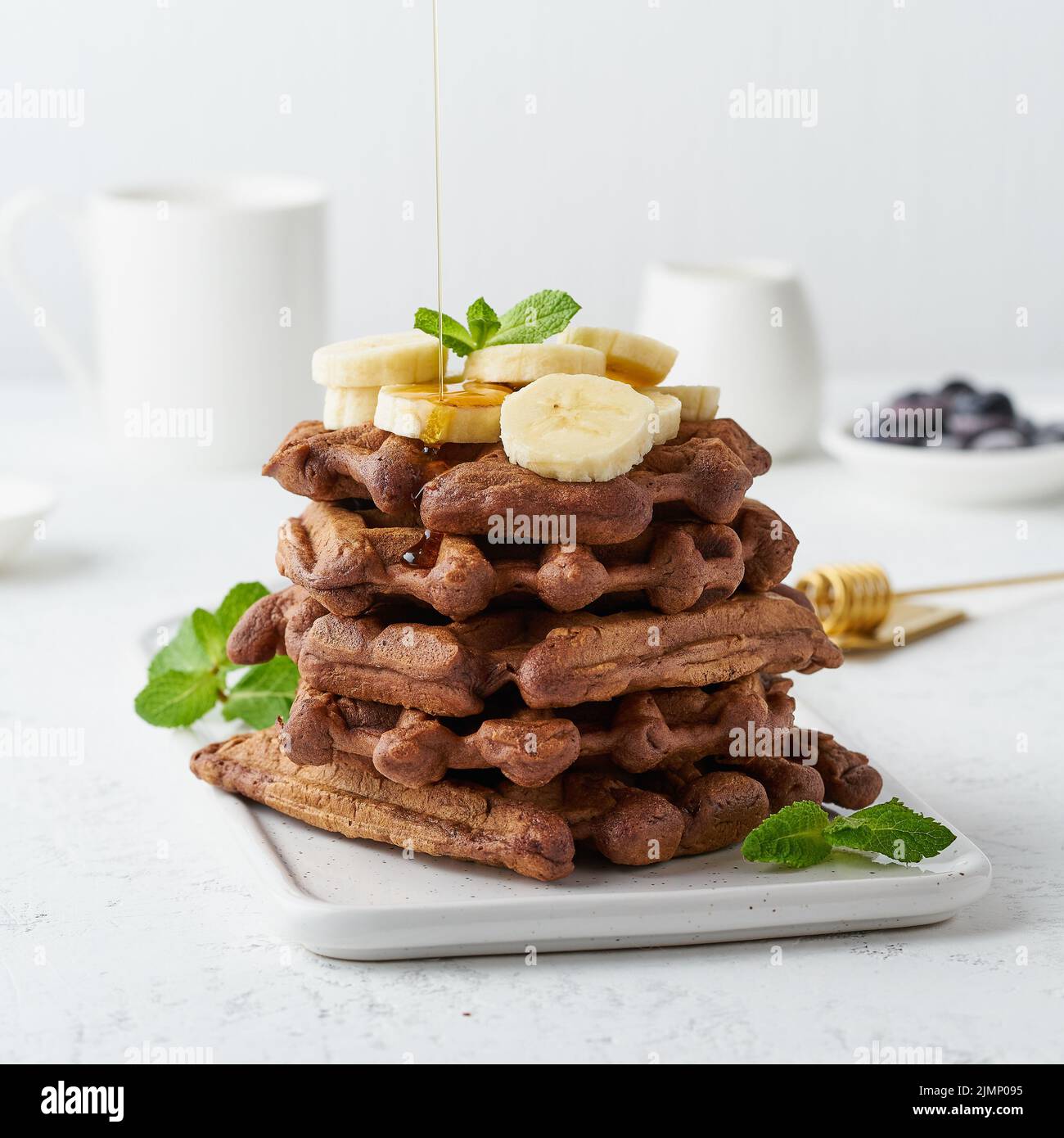 Chocolate banana waffles with maple syrup on white table, side view. Sweet brunch, maple syrup flow Stock Photo