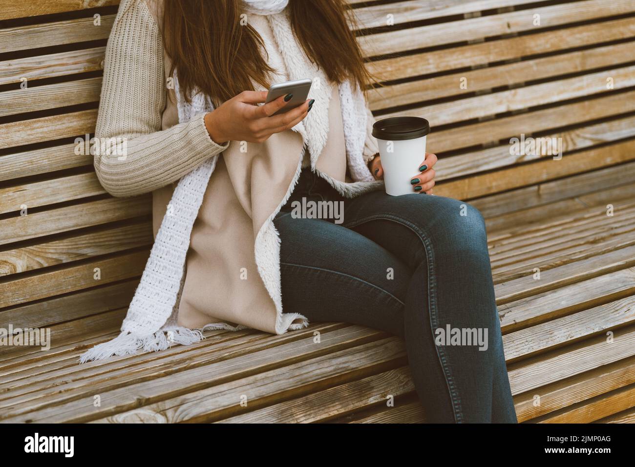 Unrecognizable beautiful young girl drinking coffee, tea from plastic mug in autumn, winter and talking on mobile phone. Woman w Stock Photo