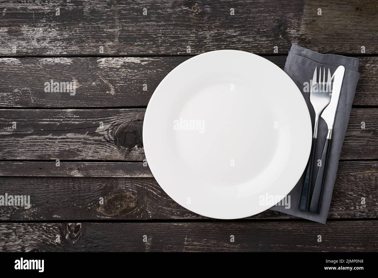 Clean empty white plate, fork and knife on gray old rustic wooden table, copy space, mock up Stock Photo