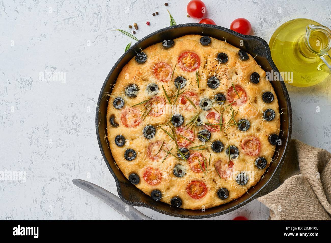 Focaccia, pizza in skillet, italian flat bread with tomatoes, olives and rosemary. Top view, copy space, white concrete backgrou Stock Photo