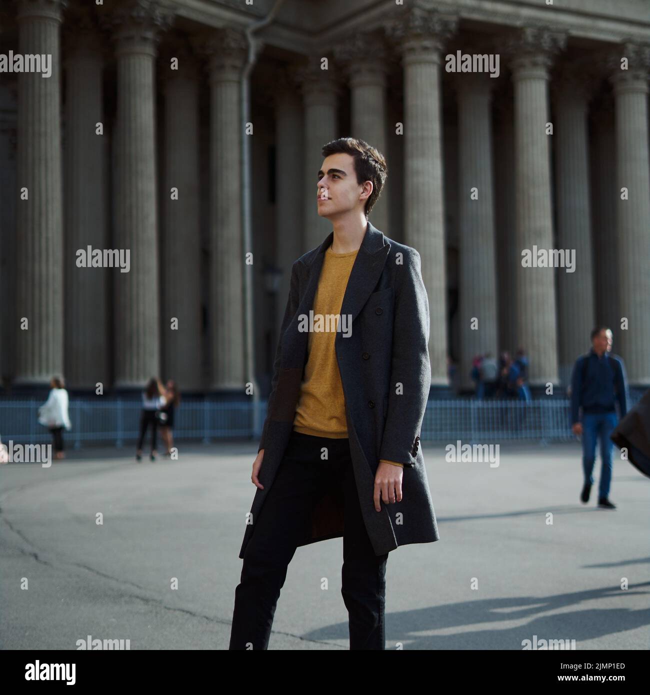 Handsome stylish fashionable man, brunette in elegant gray coat, stands on street in historical center of St. Petersburg. Young Stock Photo