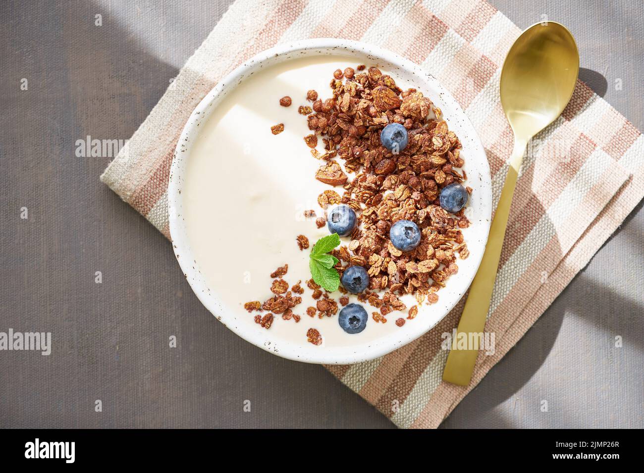 Yogurt with chocolate granola, bilberry. Breakfast on a brown table, top view, sun light Stock Photo