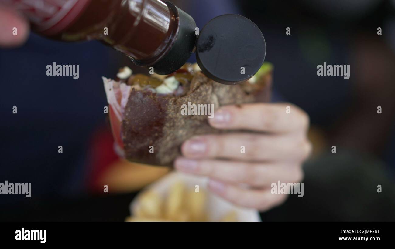 Closeup hand putting ketchup sauce on burger. Person adding hot sauce