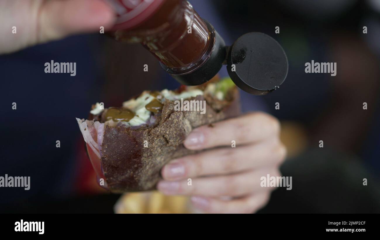 Closeup hand putting ketchup sauce on burger. Person adding hot sauce