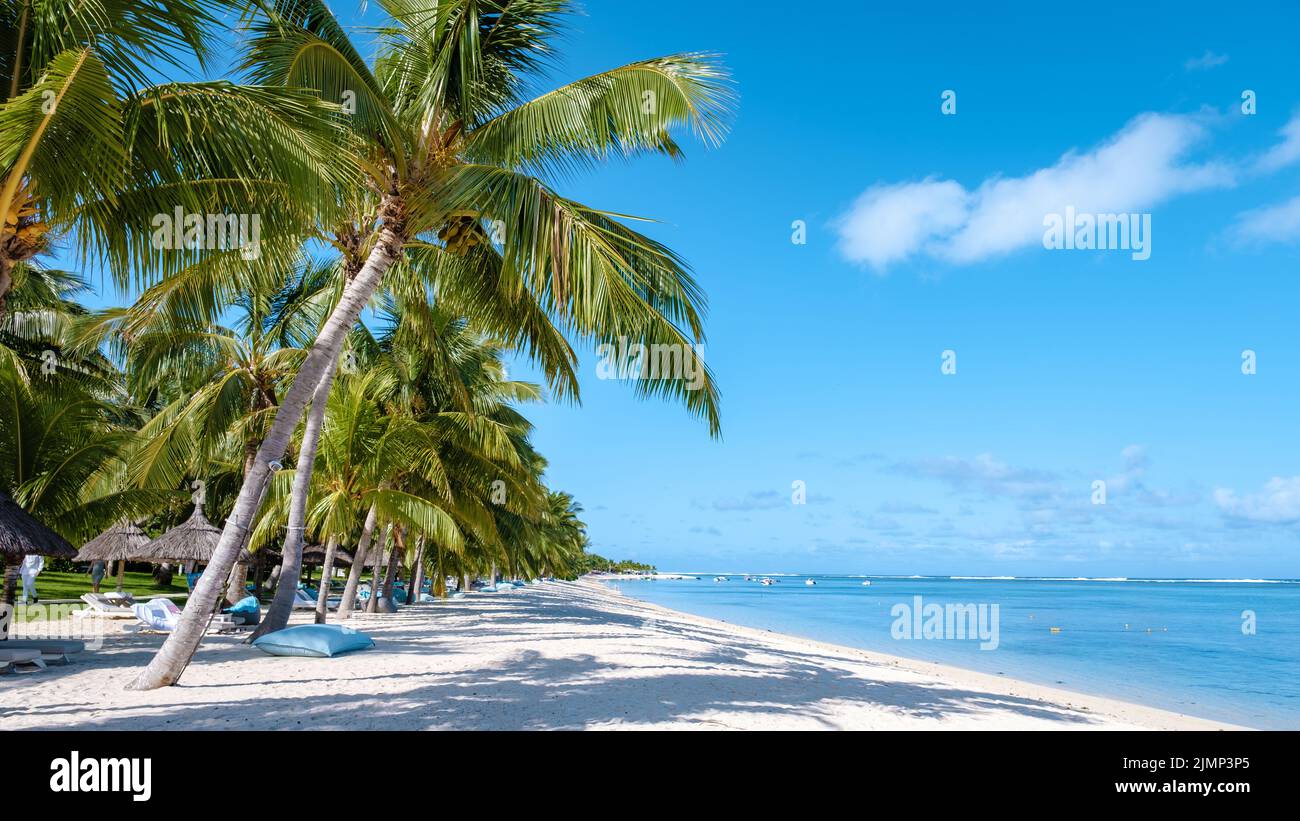 Tropical beach with palm trees and white sand blue ocean and beach beds with umbrella,Sun chairs and parasol under a palm tree a Stock Photo
