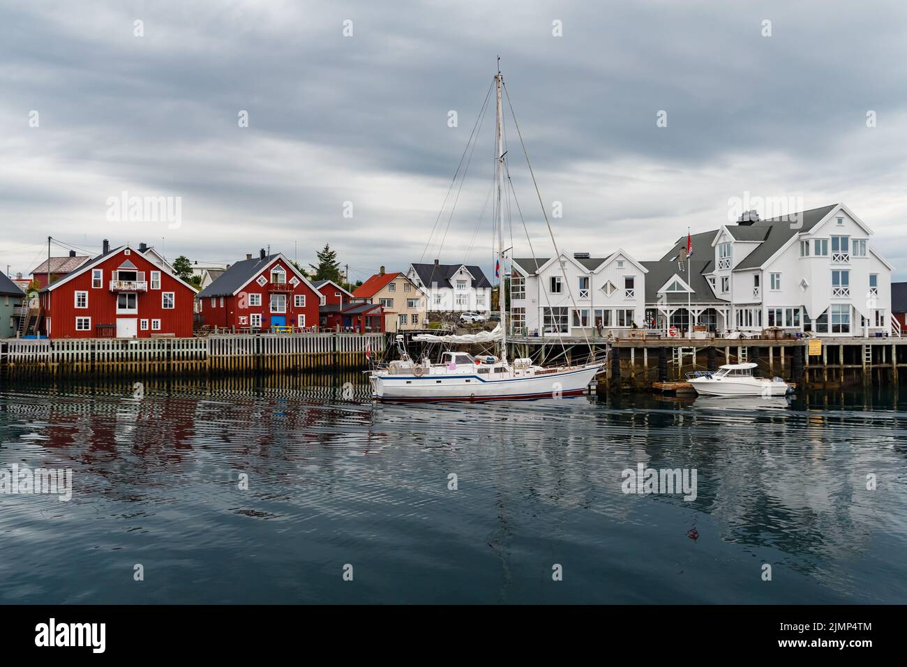 Norwegian seascape, cityscape of the town Henningsvaer, a small boat moves between peninsulas, sail boat, rocky coast with drama Stock Photo