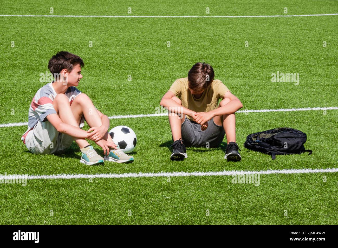 Children talking in school stadium outdoors. Teenage boy comforting consoling upset sad friend. Education, bullying, conflict, social relations Stock Photo