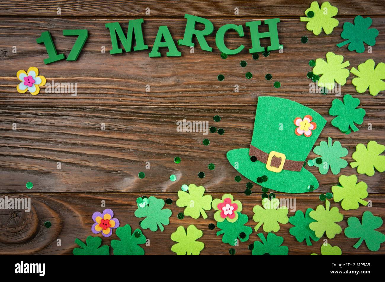 Happy Saint Patrick's mockup of handmade felt hat flowers and shamrock clover leaves on wooden table Stock Photo