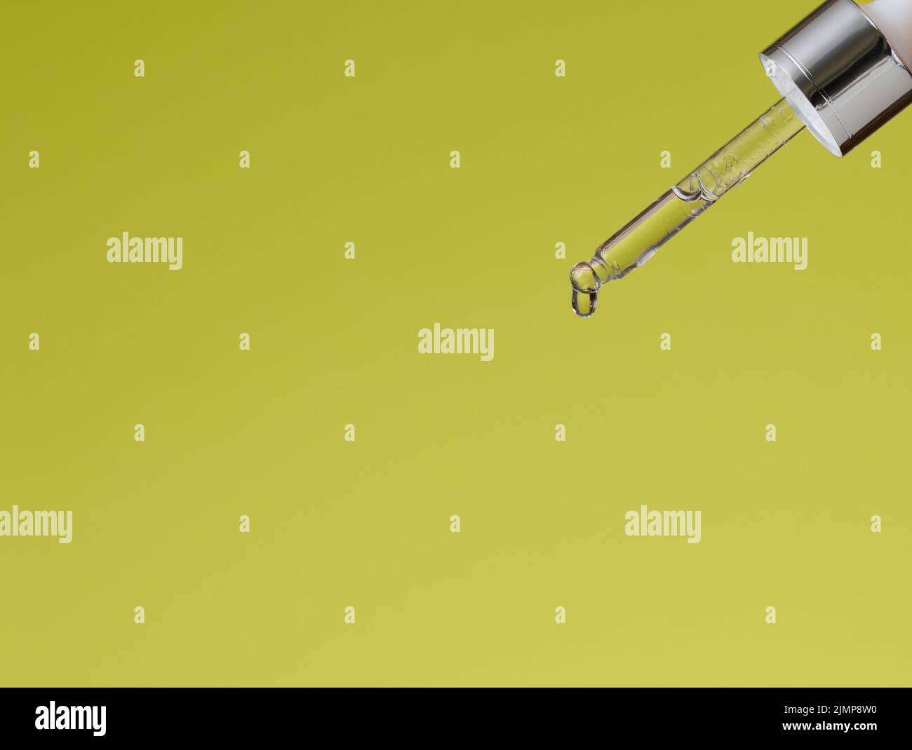 Glass pipette with dripping transparent liquid on a green background
