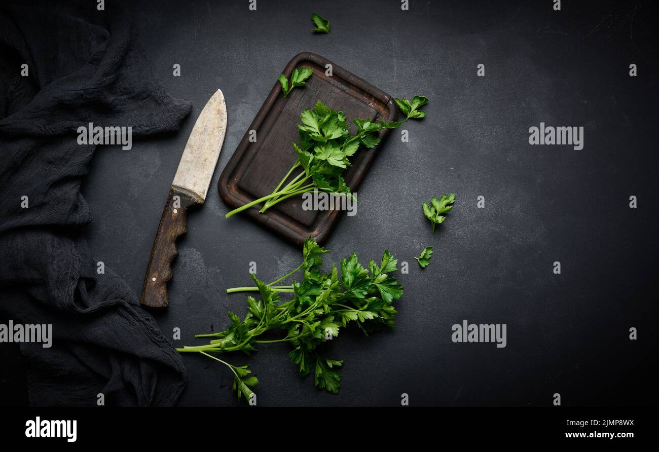Green sprigs of parsley on a wooden cutting board and a knife. Top view of black kitchen table Stock Photo