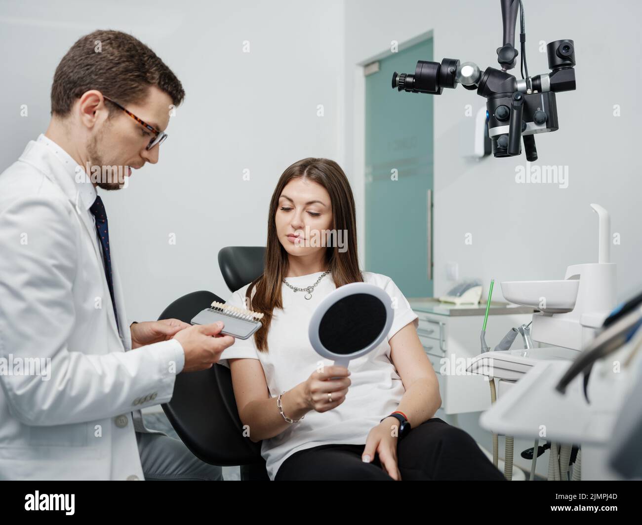 Young man dentist in white coat show veneers enamel color palette for