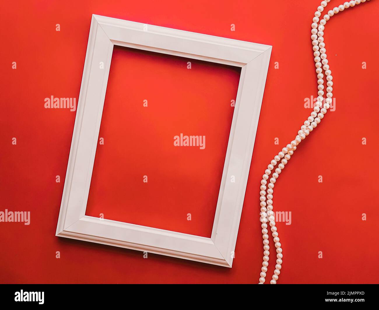 White vertical art frame and pearl jewellery on orange background as