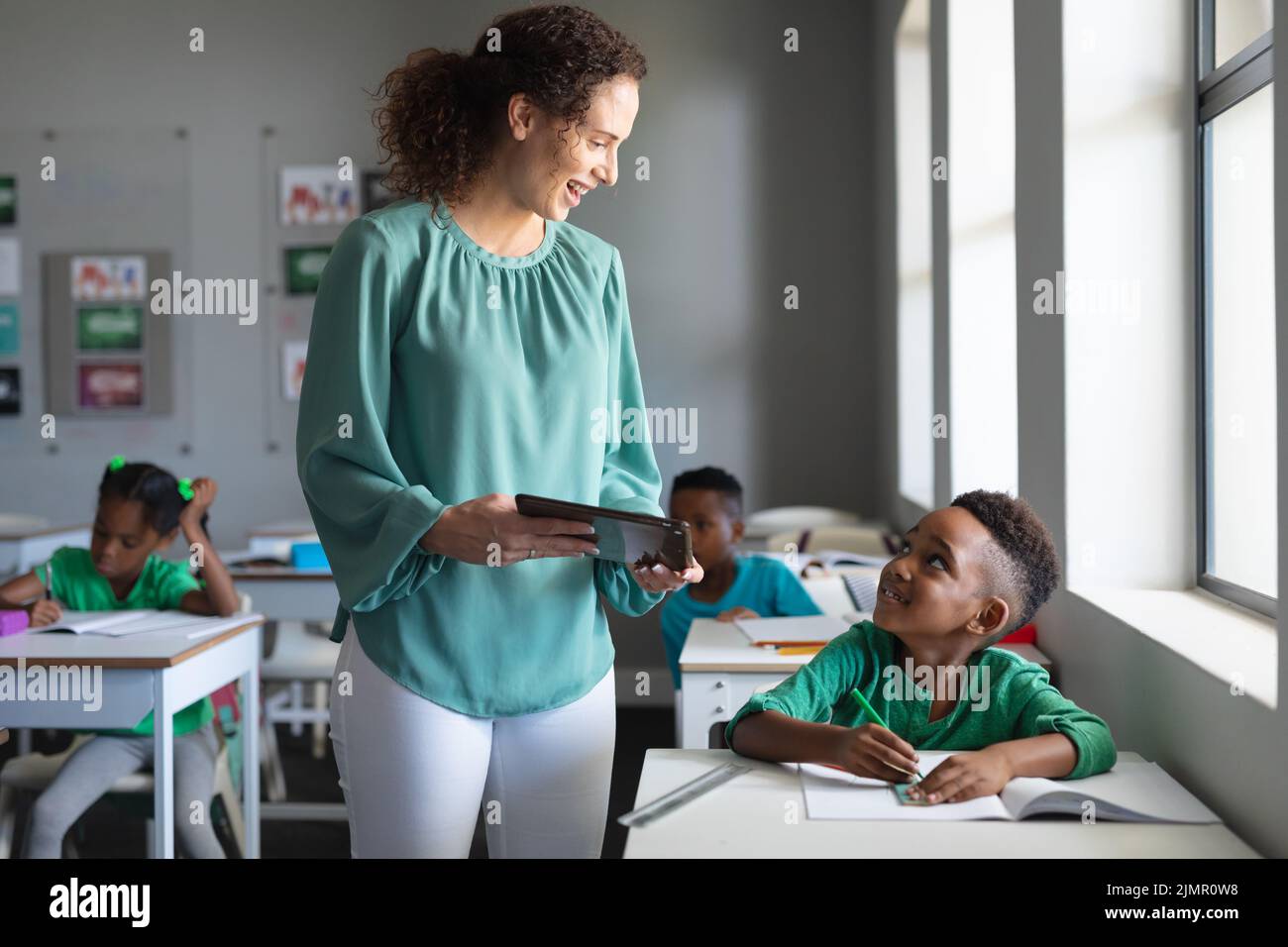 Smiling caucasian young female teacher showing digital tablet to ...