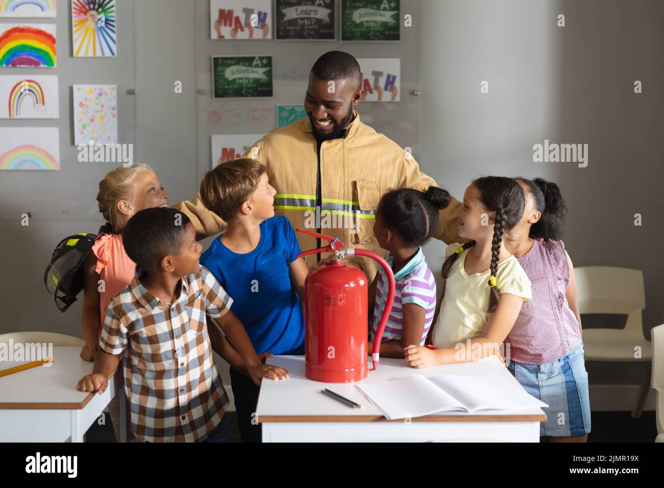 Multiracial elementary students looking african american young male teacher in firefighter uniform Stock Photo