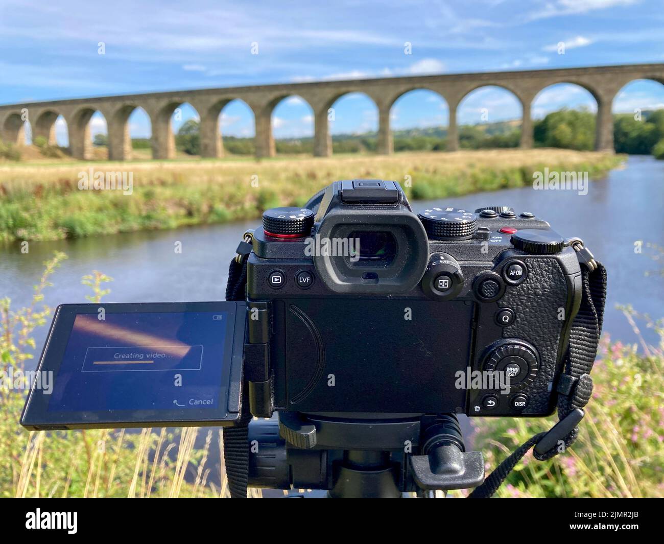 A full frame mirrorless digital camera on a tripod filming or shooting photographs whilst aimed at a beautiful landscape scene - Arthington Viaduct. Stock Photo