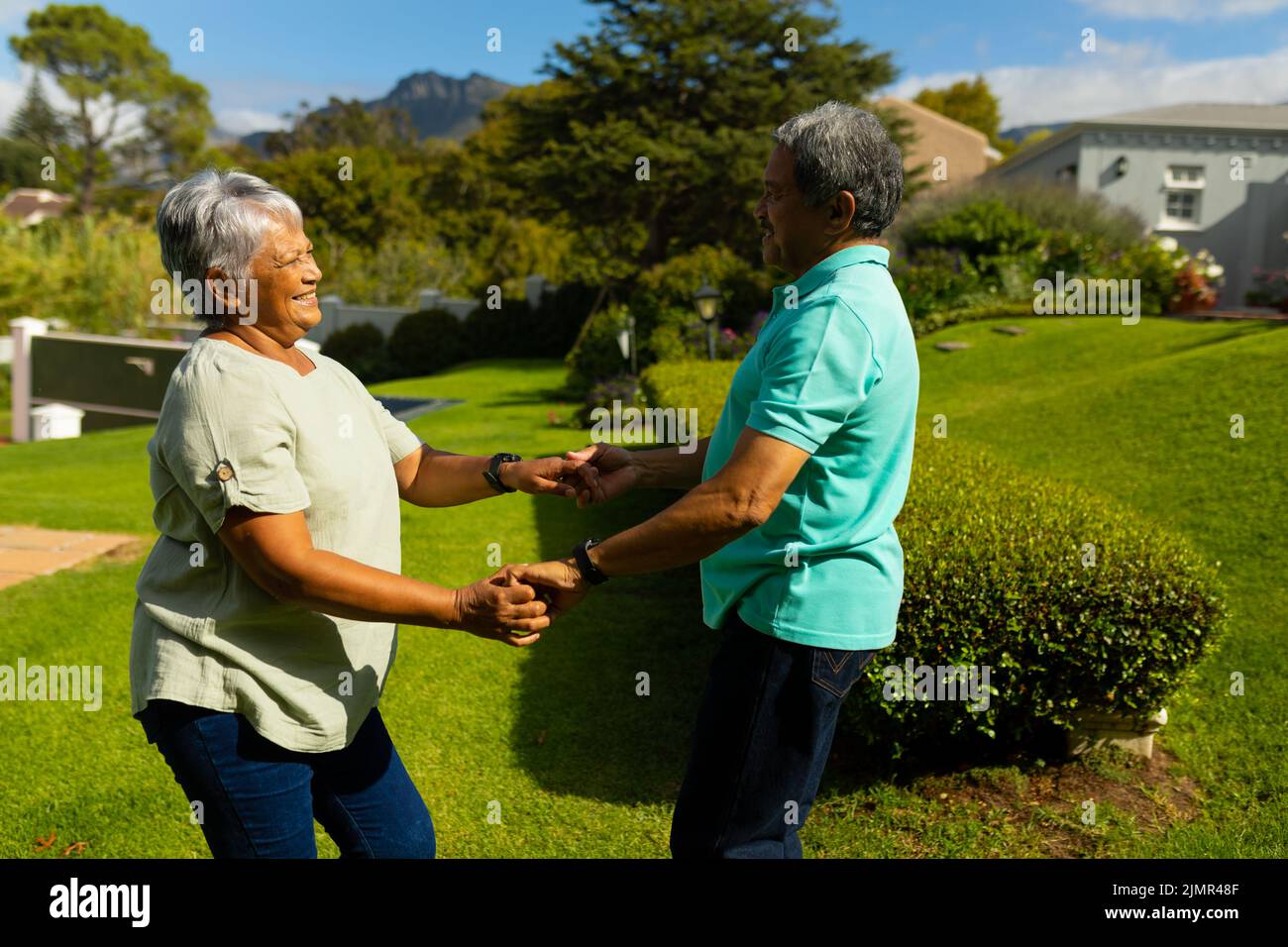 Side view of happy biracial senior couple holding hands and dancing in park during sunny day Stock Photo