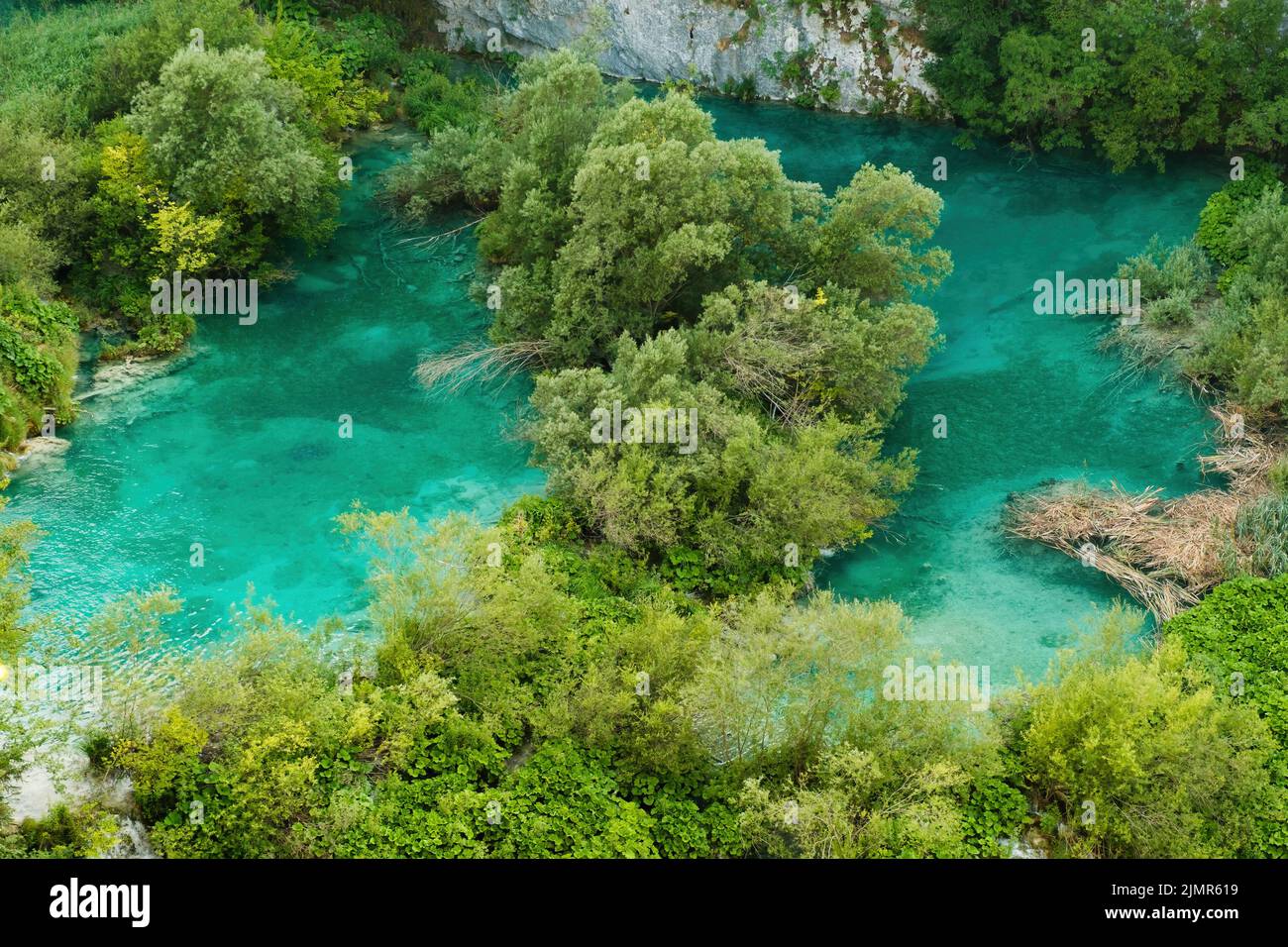 Small green islands among turquoise-colored transparent water of lake surrounded by mountains. Breathtaking landscape of natural reserve on Plitvice lakes upper view Stock Photo