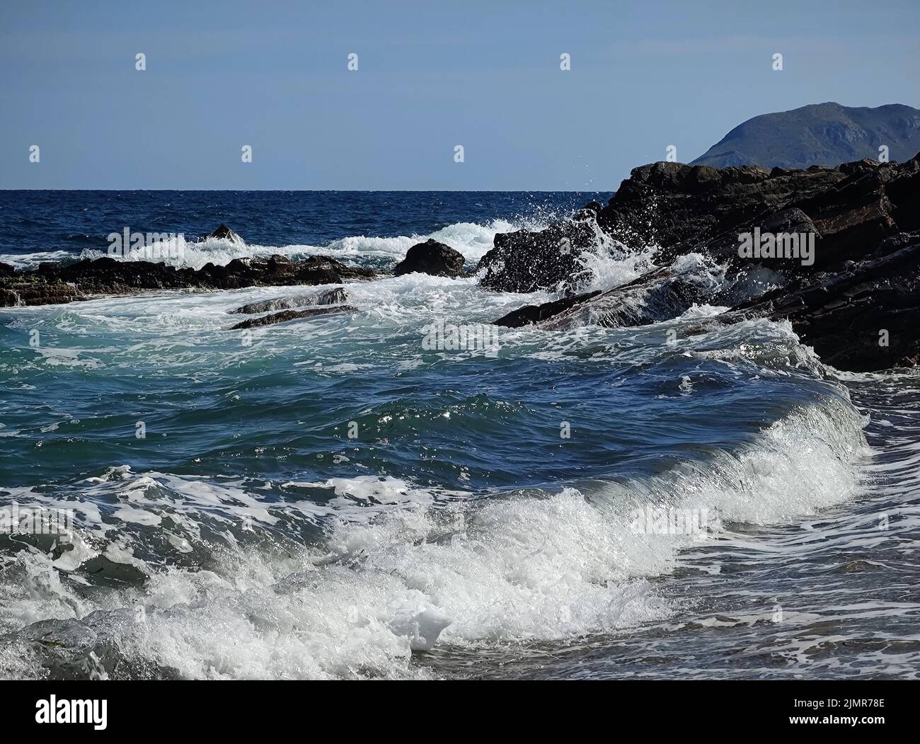 summer fun dynamic waves breaking on rocks blue sky and sunshine Stock Photo