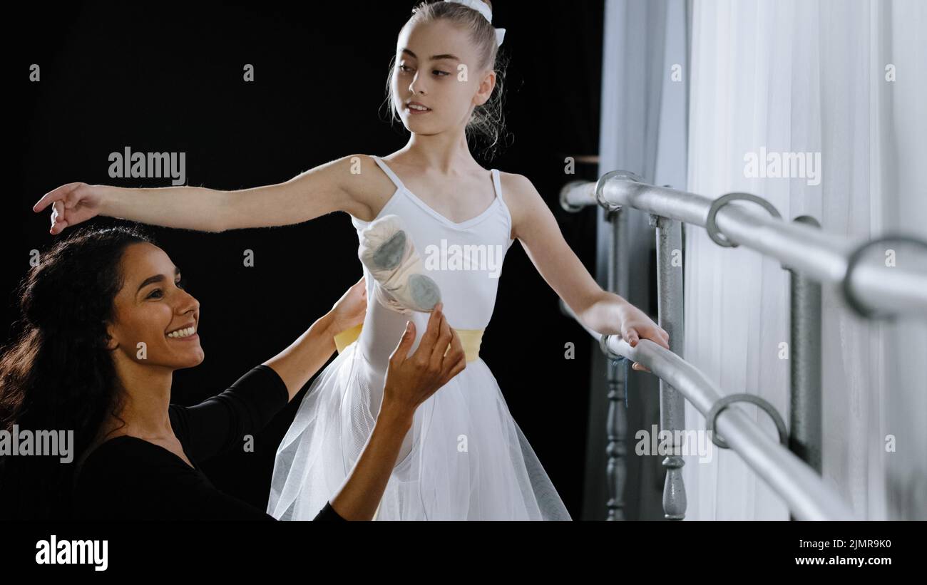 Girl teenager ballerina student doing classic exercises near ballet barre trains listens to advice of woman teacher professional female trainer helps Stock Photo