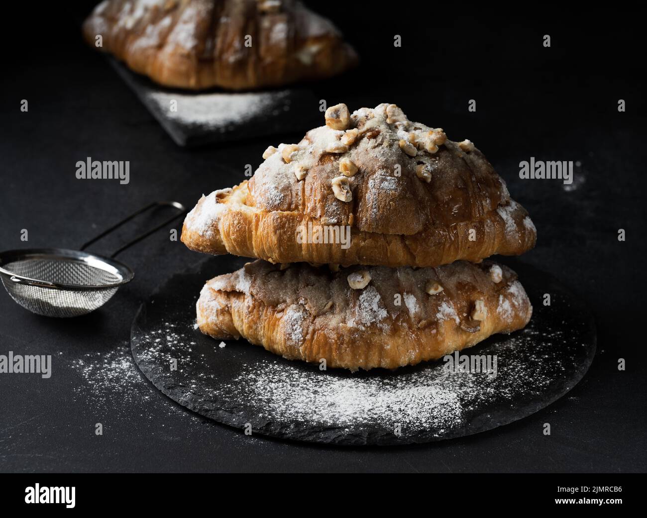 Baked croissant on a wooden board and sprinkled with powdered sugar, black table. Appetizing pastries for breakfast Stock Photo