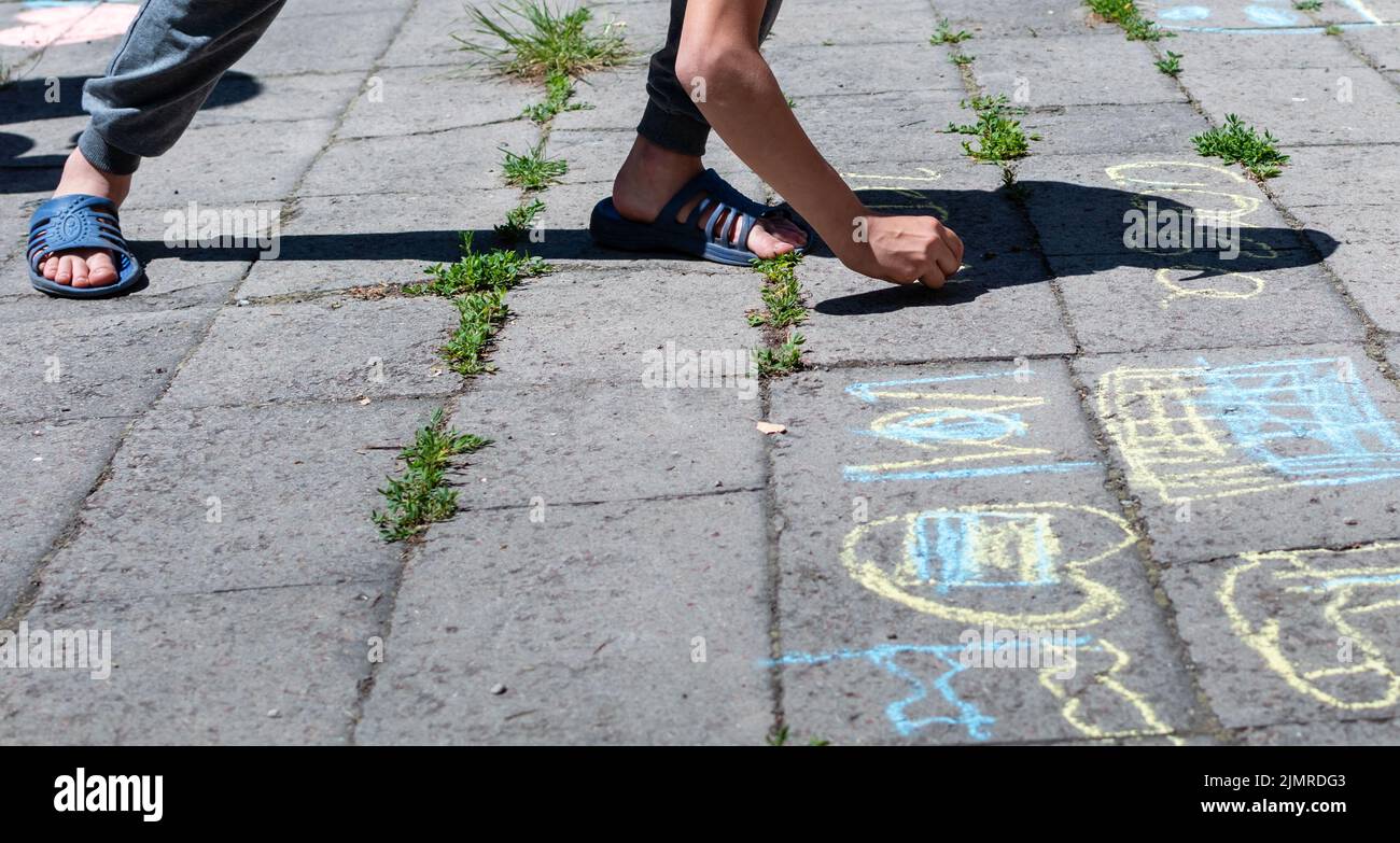 Boy writing with colored chalk on pavement in summer time Stock Photo