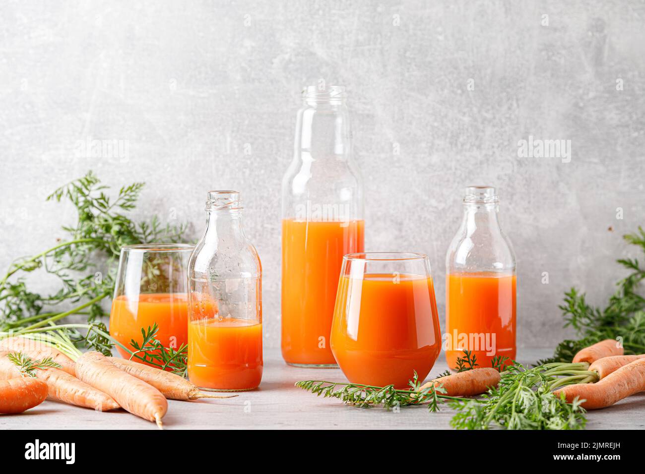 Carrot juice in a glass and bottle and fresh carrots with leaves Stock