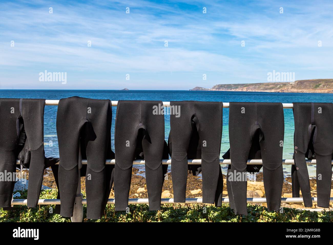 Wet suits hanging to dry on a railing, at Sennen beach in Cornwall