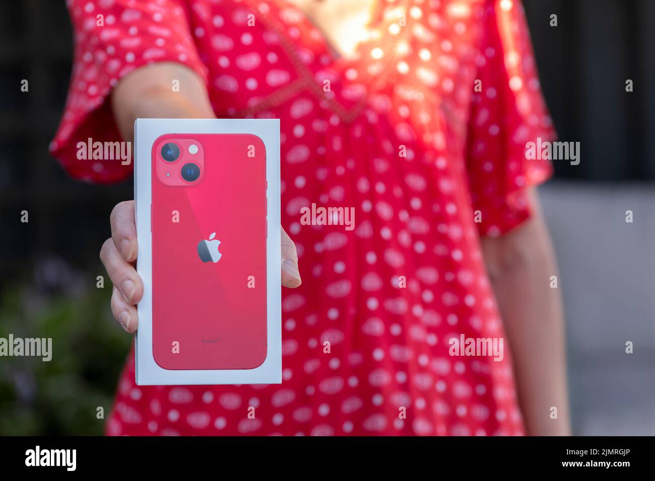 A female, a middle aged woman holding a new Apple iPhone 13 box with her new iPhone purchase inside the box. It’s a red model as shown in the image Stock Photo