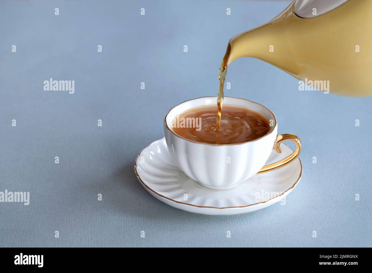A fresh brew of tea being poured from a traditional English china tea pot into a bone china cup on a saucer. It’s a strong brew with a little milk Stock Photo