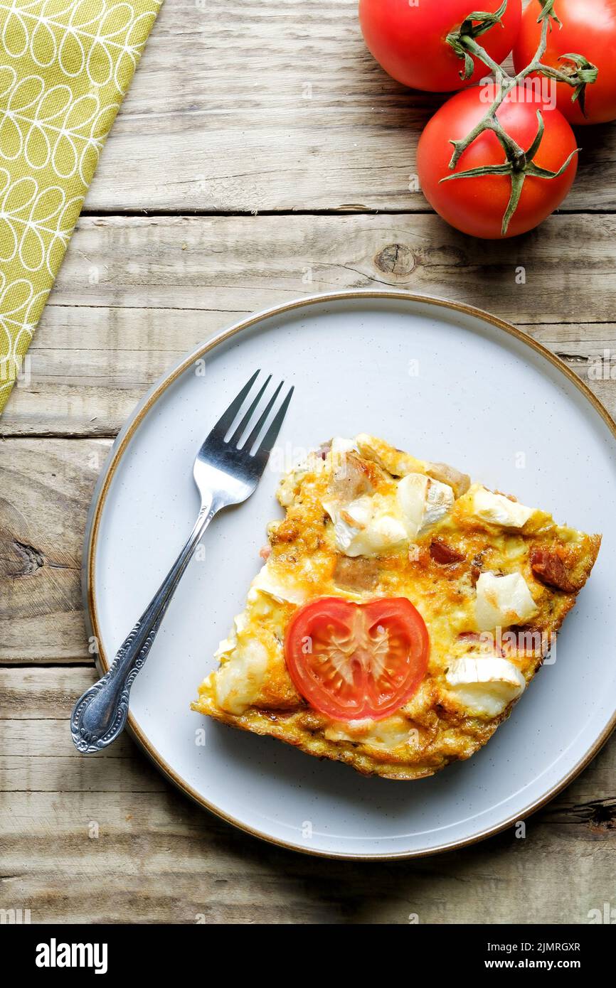 A slice of freshly made Goat Cheese Frittata. An egg based healthy eating option. The frittata is plated and rests on a wooden table Stock Photo