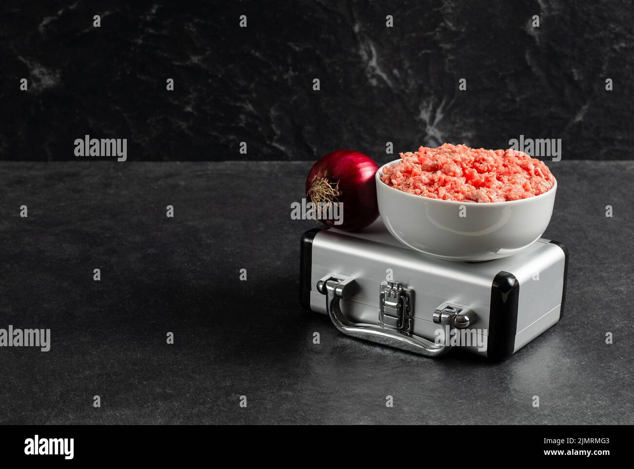 Plate with fresh ground beef, silver suitcase, red onion on a grey black background, stock photo Stock Photo