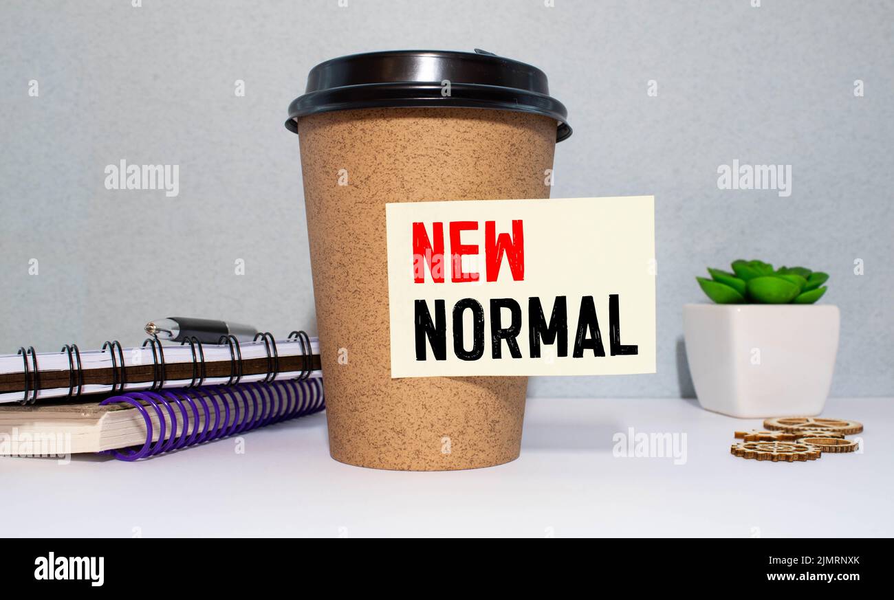NEW NORMAL inscription in a white notebook near a cup of coffee on a black background Stock Photo