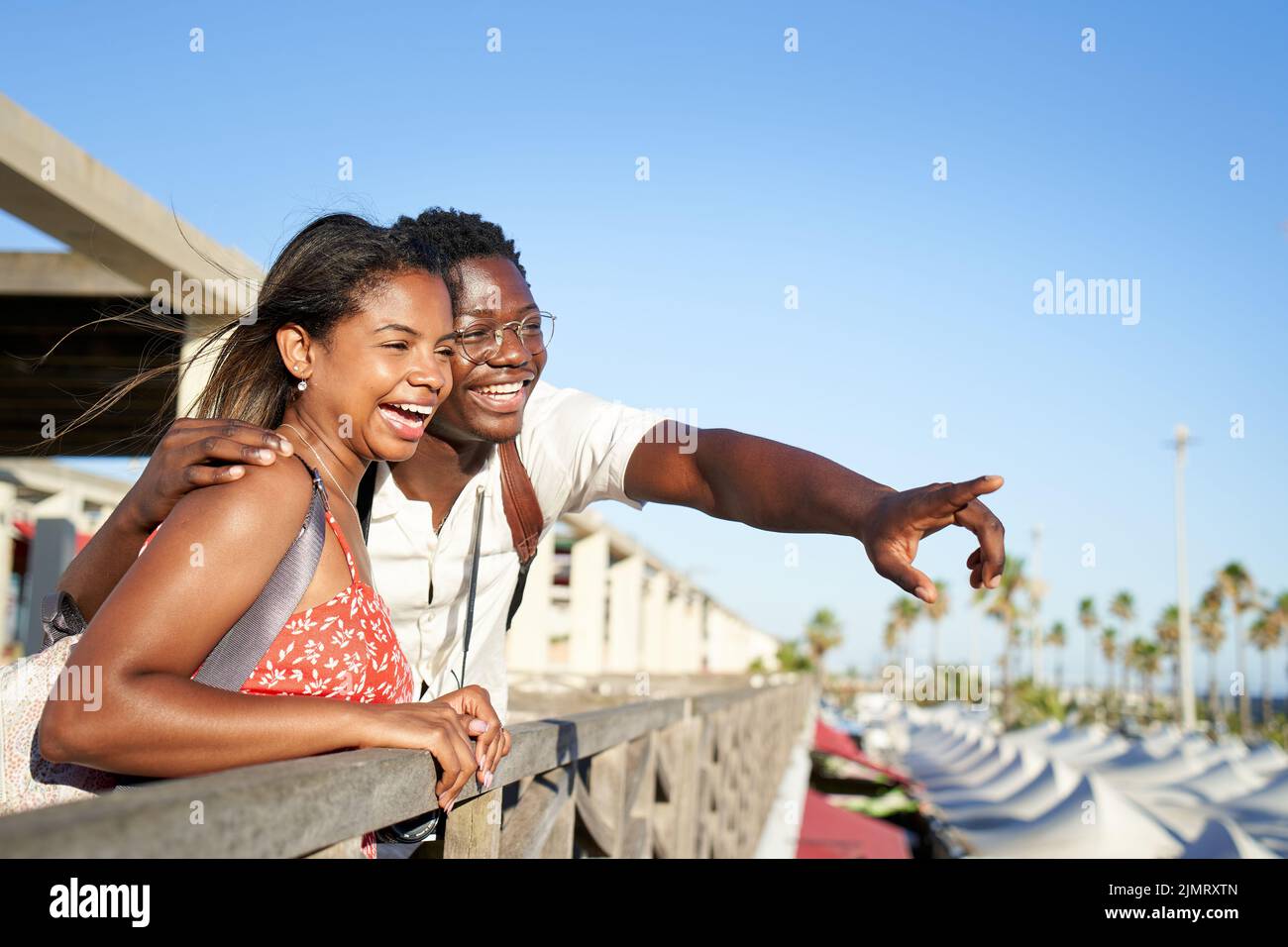 Beautiful couple of African origin have fun embracing in a coastal city center, leaning out of a gazebo pointing to the horizon. Background with copy Stock Photo