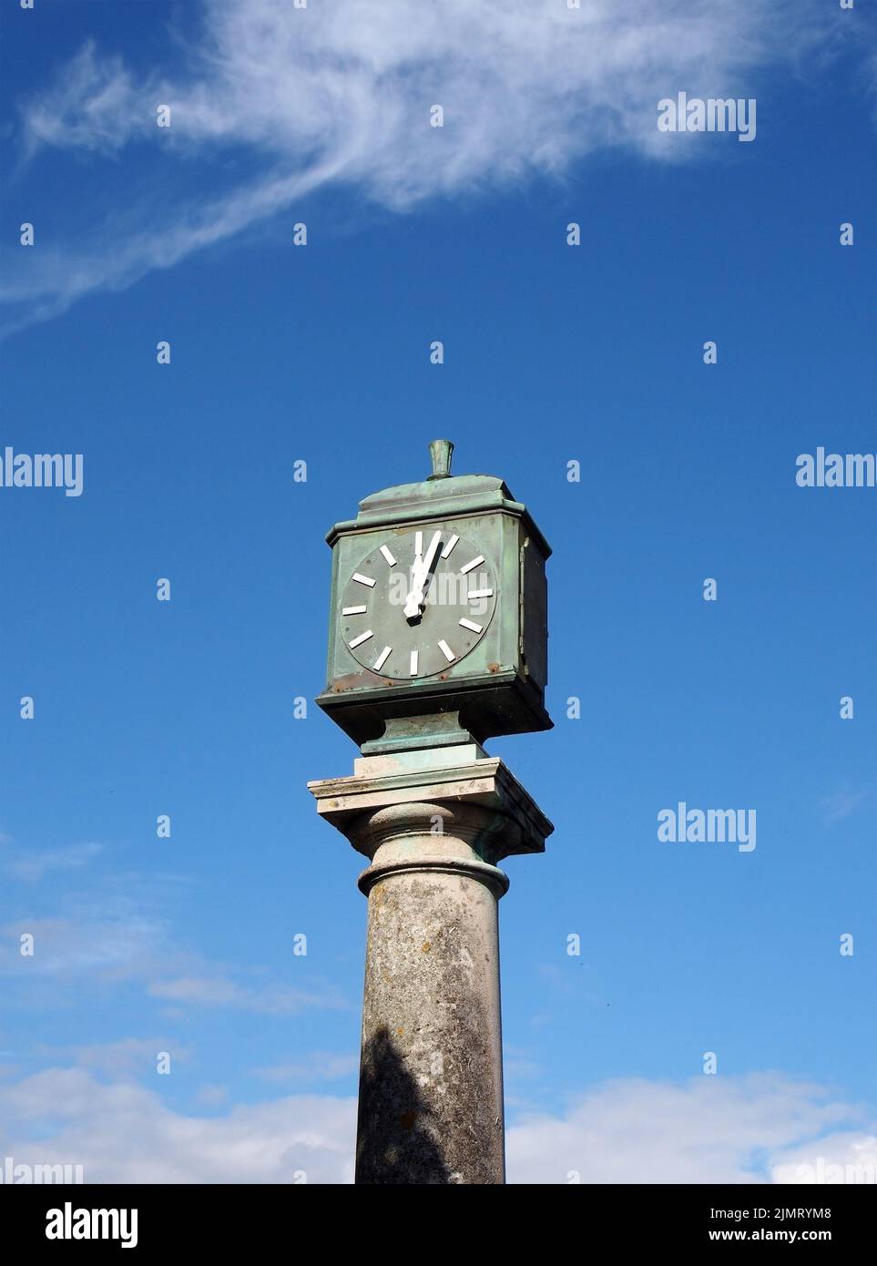 Old green metal outdoor clock on a stone pillar in arnside cumbria against a blue cloudy sky Stock Photo