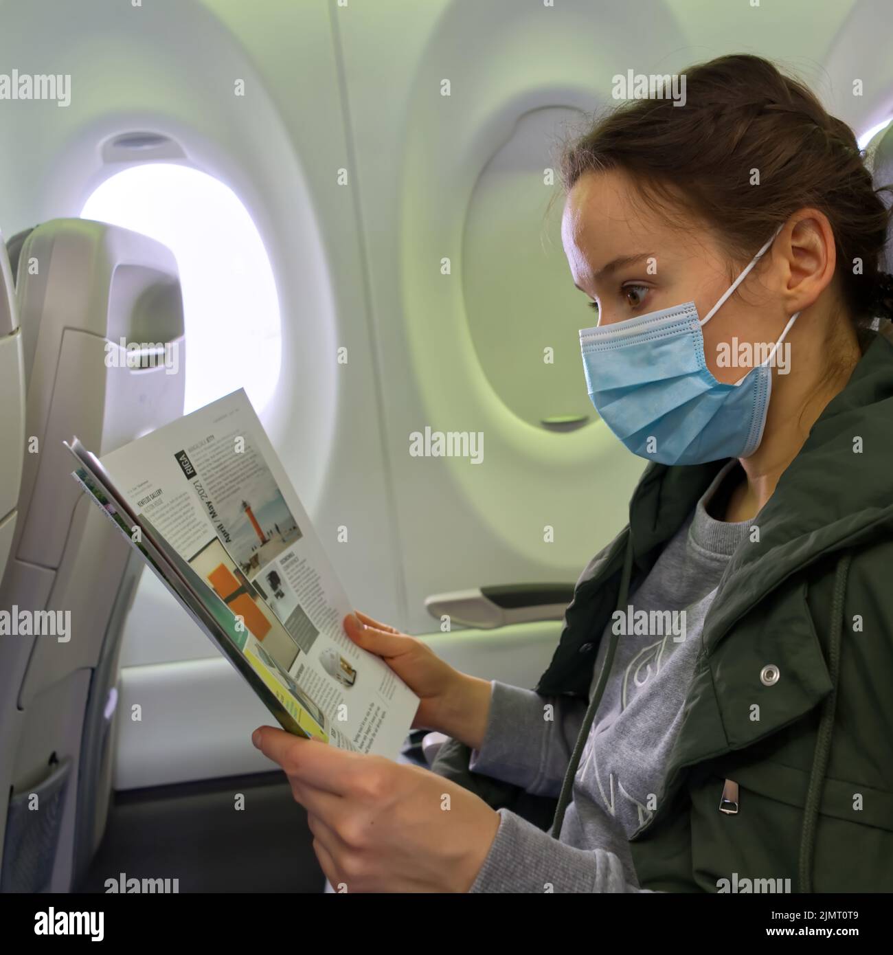 female traveler wearing a mask to prevent covid-19 infection while traveling on an airplane watching a magazine Stock Photo