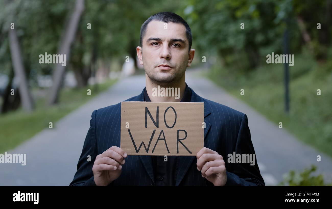 Serious strong caucasian adult man activist standing outdoors demonstrating cardboard plate with words no war protesting against the Russian invasion Stock Photo