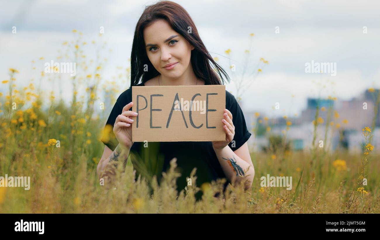 Beautiful female activist caucasian woman girl stands outside flip paper cardboard shows at camera banner with lettering word peace painted slogan Stock Photo