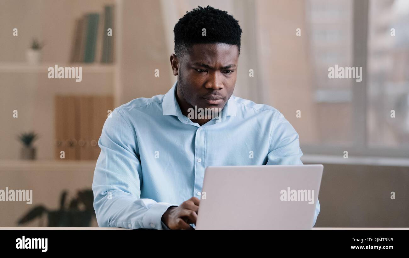 Angry guy annoyed african american man male boss worker dissatisfied has problem with computer system work feels wrath aggression with unsuccessful Stock Photo