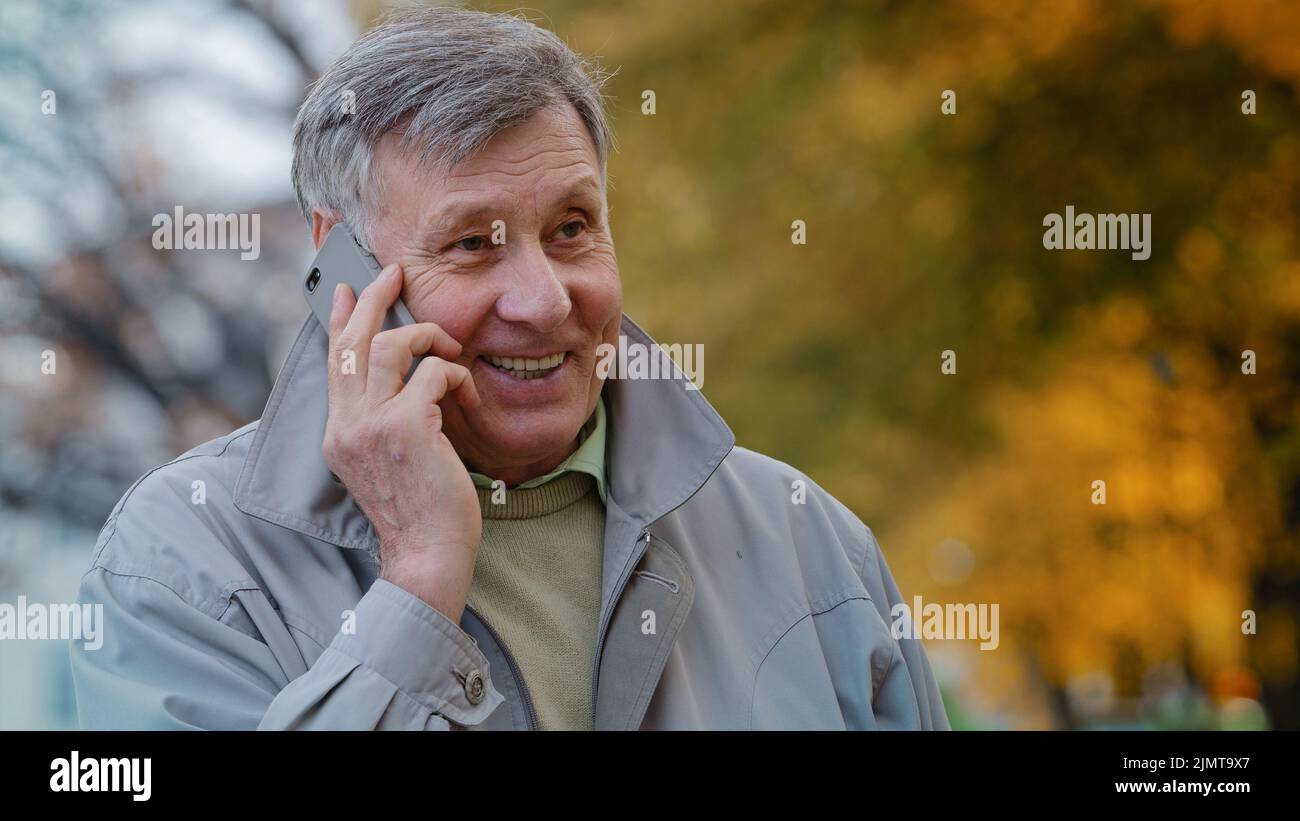 Portrait mature elderly man pensioner communicate remotely using modern smartphone talking family or friends order delivery happy old senior laughing Stock Photo