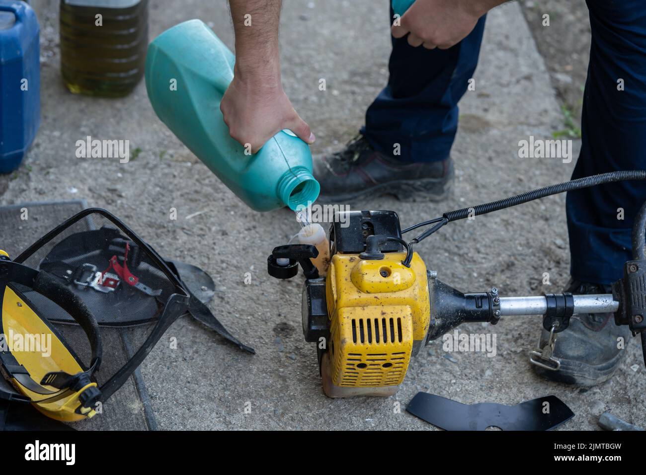 Young farmer adding petrol gas to the gasoline tank of the brushcutter string trimmer Stock Photo