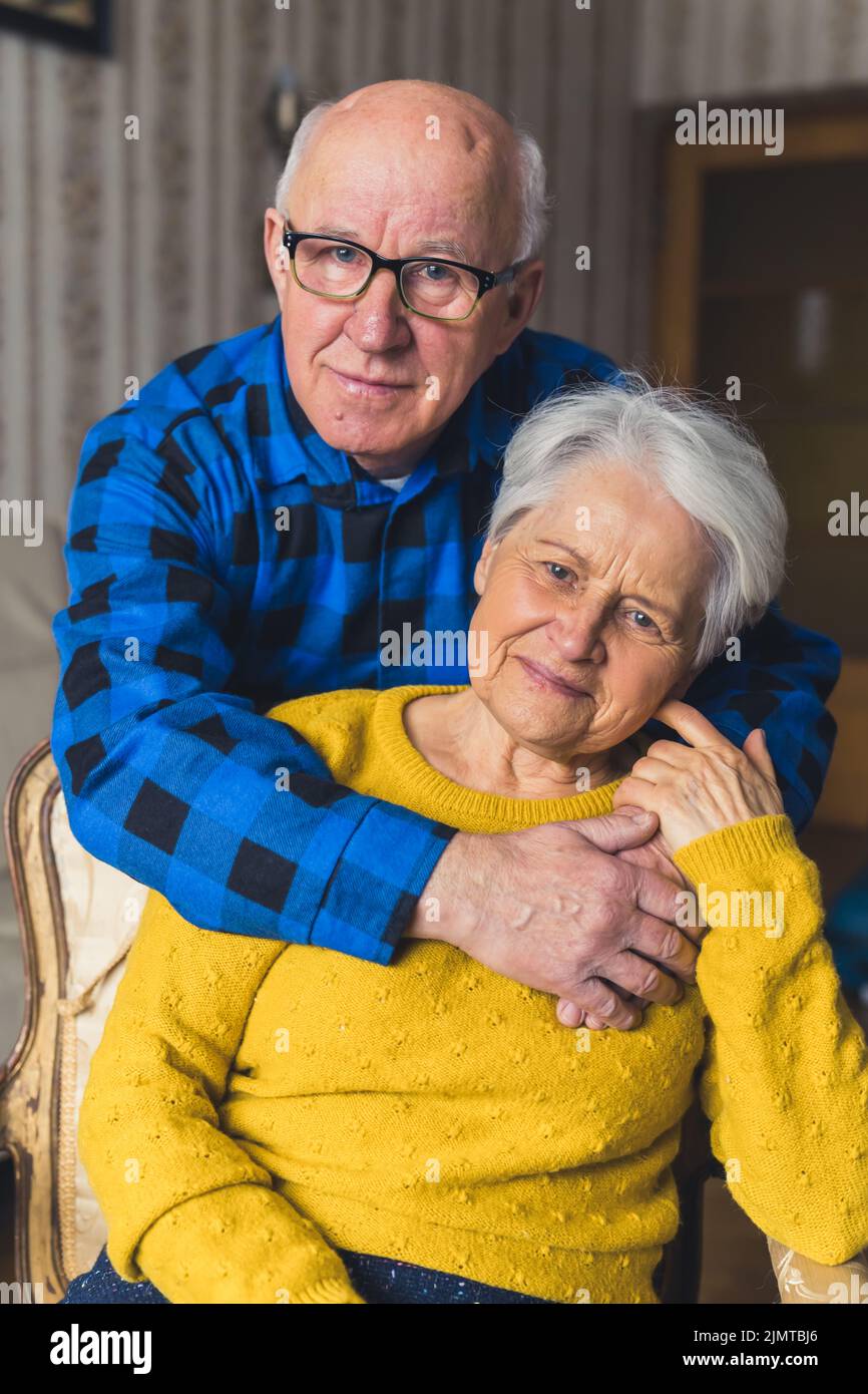 Portrait Of An Elderly Couple Caring Husband Standing Behind His Happy Loving Wife And Hugging