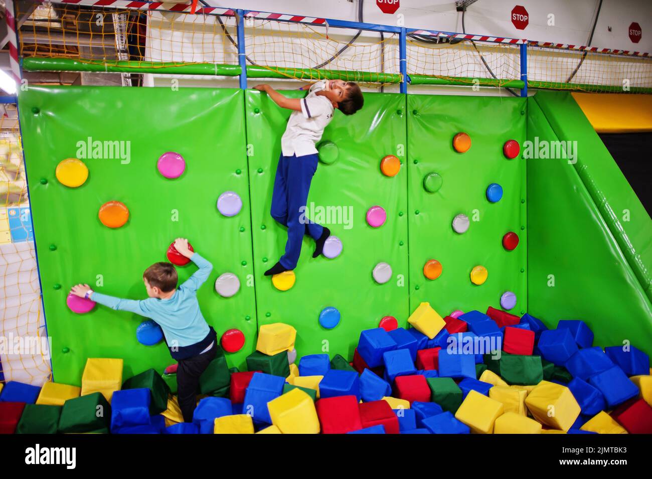 Two brothers kids climbing on a green wall in attraction playground. Stock Photo