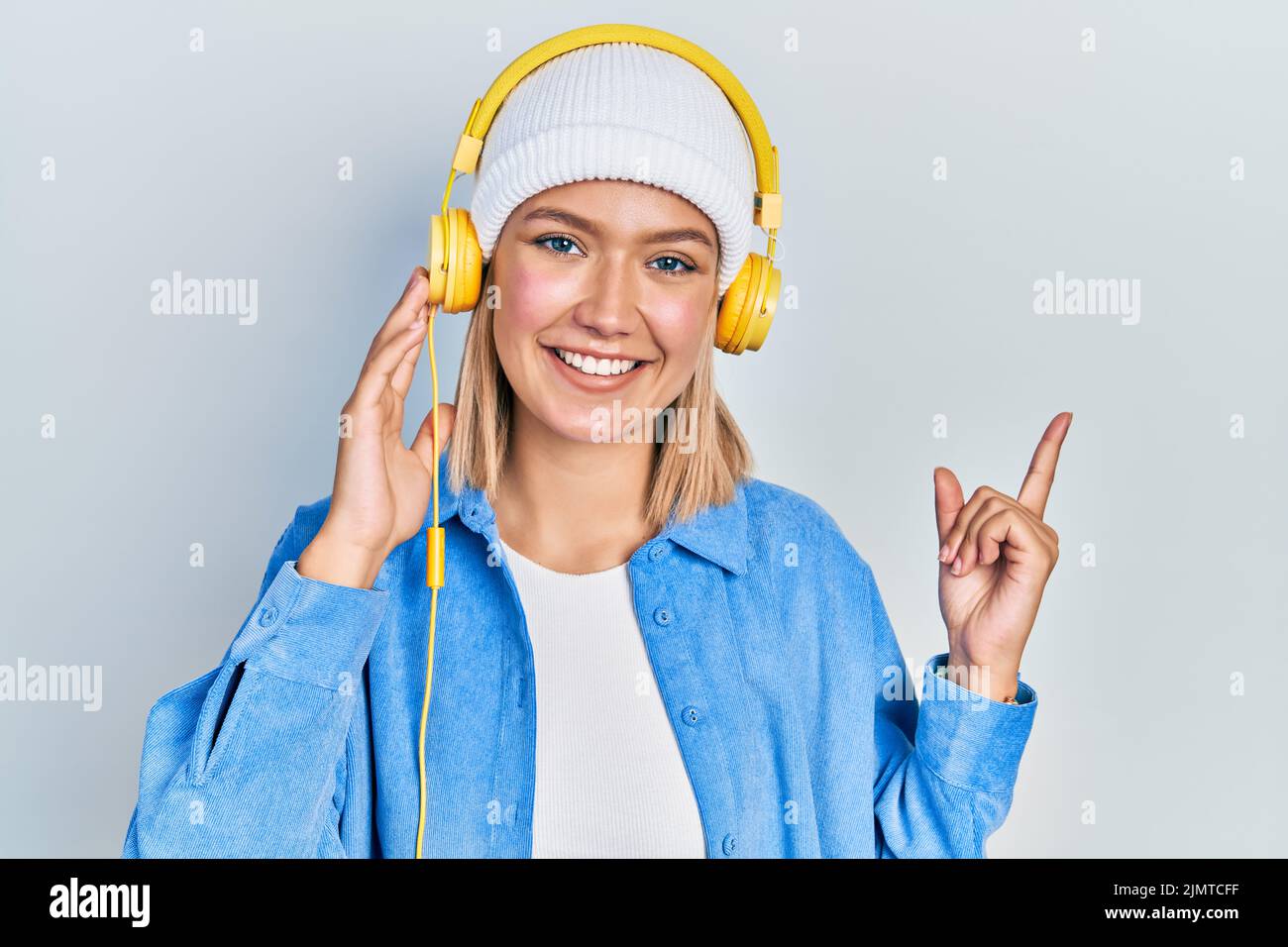 Beautiful blonde woman listening to music using headphones smiling ...