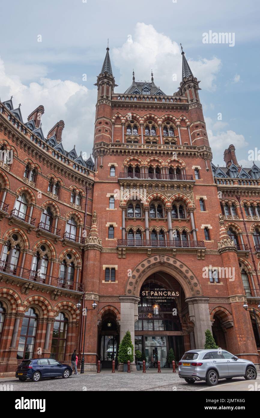 London, Great Britain - July 3, 2022: Central entrance tower on red brick historic St. Pancras Renaissance Hotel facade under blue cloudscape with car Stock Photo