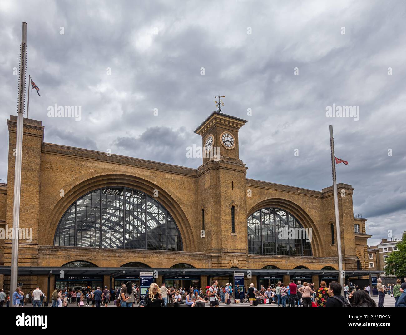 London, Great Britain - July 3, 2022: Closeup, Yellow brick King's Cross railway station with clock tower separating 2 wings under dark gray cloudscap Stock Photo
