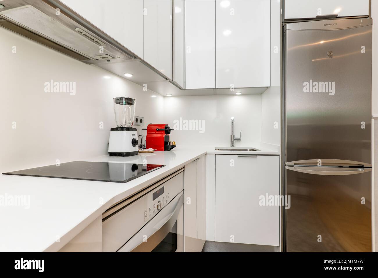 Corner of an open plan kitchen with a white worktop, ceramic hob, sink
