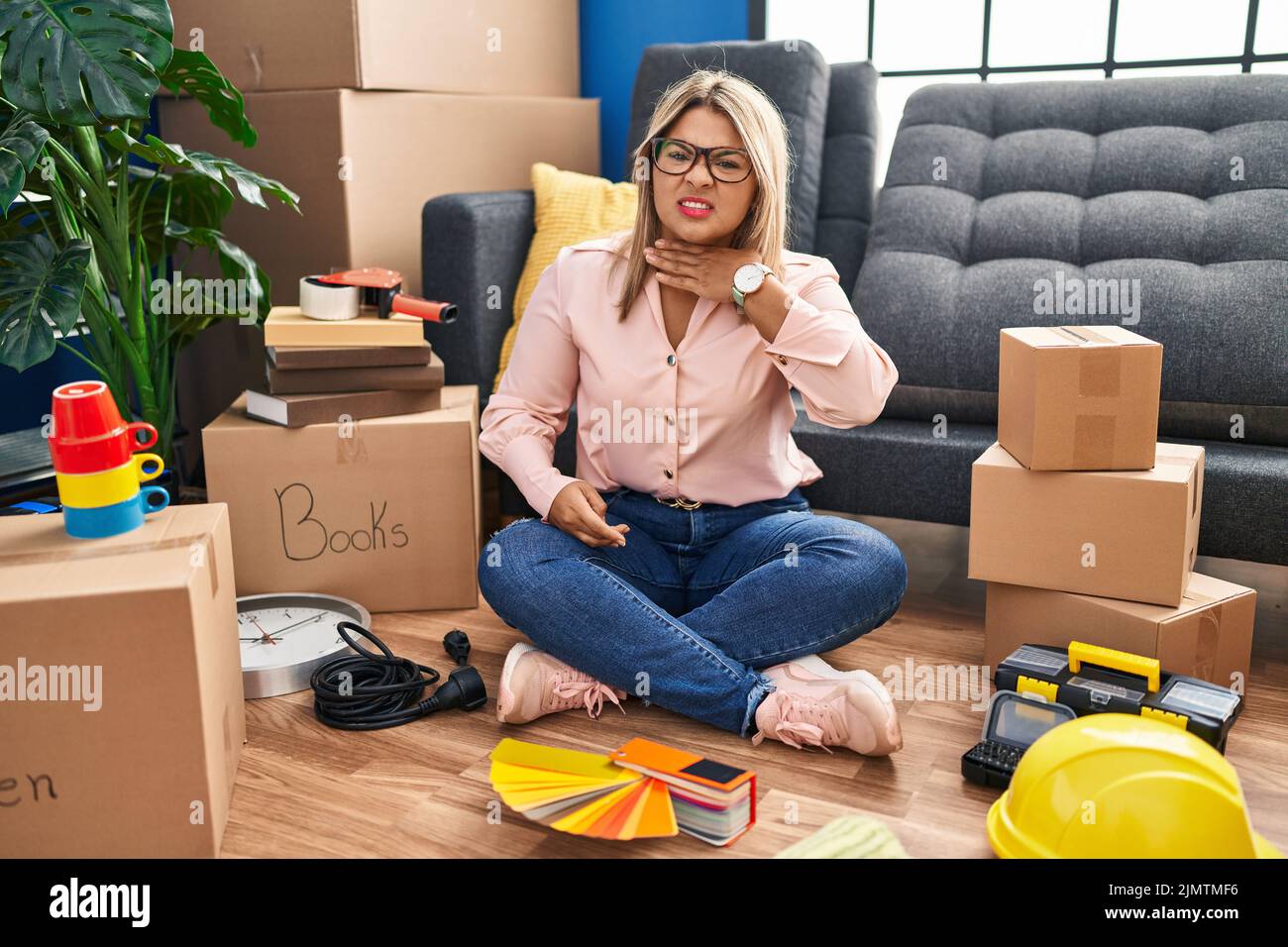 Young hispanic woman moving to a new home sitting on the floor cutting throat with hand as knife, threaten aggression with furious violence Stock Photo