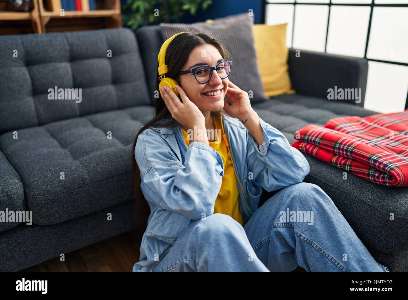 Young hispanic woman listening to music sitting on floor at home Stock ...